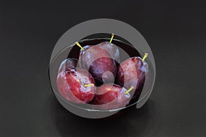 Fresh plum. Autumn harvest. Ripe purple plums in glass bowl on dark background. Concept: seasonal fruits, healthy food. Top view.