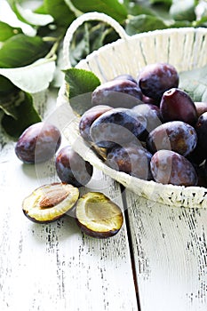 Fresh plums in basket on white wooden background