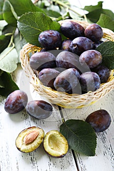 Fresh plums in basket on white wooden background.