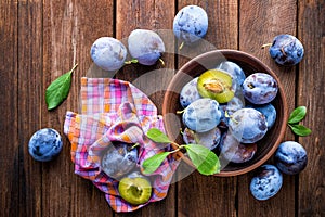 Fresh plums with green leaves on wooden rustic background