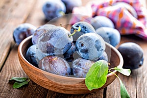 Fresh plums with green leaves on wooden rustic background