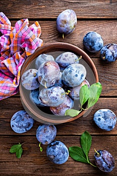 Fresh plums with green leaves on wooden rustic background