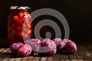 Fresh plums and a jar of plum compote on a dark wooden table, selective focus on the central plum, shallow depth of field