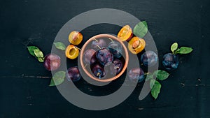 Fresh plums with leaves. Fruits. On a black wooden background. Top view.