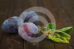 Fresh plums with leaves on wooden background