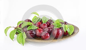Fresh plums with leaves on a wooden plate close-up. Copy space