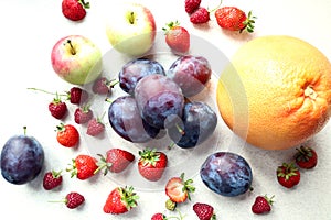 Fresh plums with strawberries with apples and citrus fruits, close - up, top view-the concept of cooking delicious dishes from