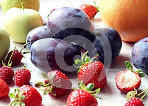 Fresh plums with strawberries on the background of apples and citrus, close - up, side view-the concept of cooking delicious