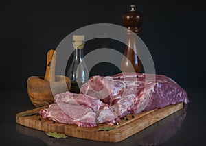 Fresh pork flesh with incised portions for frying lies on a cutting board on a black background