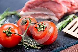 Fresh pork meat with ingredients for cooking on dark background. Tomato and rosemary