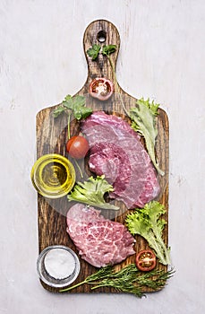 Fresh pork steak with salad, tomato, oil and salt on a cutting board wooden rustic background top view close up