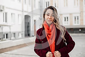 Fresh portrait young woman in vintage burgundy coat with fashionable orange scarf on street in city. Pretty beautiful girl model