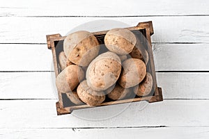 Fresh potatoes in crate on white wooden table.