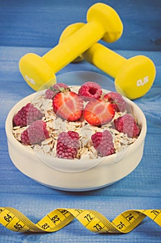 Fresh prepared oat flakes with fruits, dumbbells and centimeter, slimming and healthy lifestyle concept