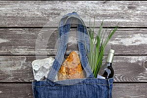 Fresh produce in blue denim market bag on wooden background, flat lay. Eco friendly reusable shopping bag for minimize waste,