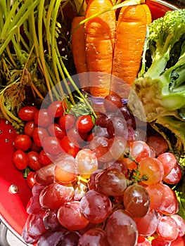 Fresh produce - carrots broccoli cherry tomatoes and grapes - closeup in a red colander