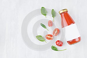 Fresh pulpy tomato juice in glass bottle with blank label, ingredients and green spinach leaves on white wood board, mock up for d