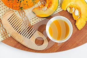 Fresh pumpkin juice in a small white bowl and wooden hair brush. Homemade beauty treatment and spa recipe. Top view