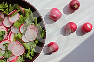 Fresh radish, lettuce and parsley salad in a brown ceramic bowl on a white wooden background