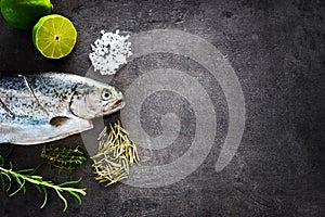 Fresh rainbow trout with lime and seasoning. Fish at dark background. Detail of preparation