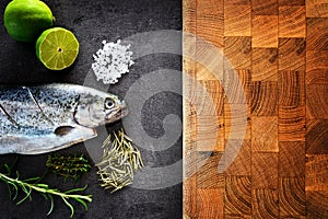 Fresh rainbow trout with lime and seasoning. Fish at dark background. Detail of preparation