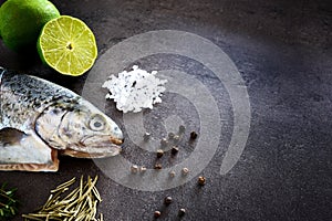 Fresh rainbow trout with lime and seasoning. Fish at dark background. Detail of preparation