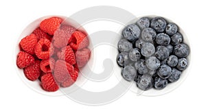 Fresh raspberries and blueberries, whole and ripe fruits, in white bowls