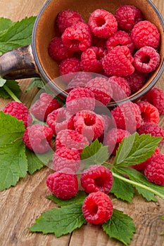 Fresh raspberries with leafs in bowl on wooden table