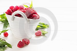 Fresh Raspberries in the white bowl with green leaves,white wooden board