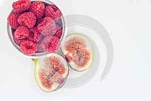 Fresh raspberries in white ceramic bowl and Brown turkey figs isolated on gray background.