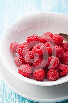 Fresh raspberries in a white ceramic bowl with metal spoon