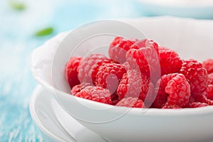 Fresh raspberries in a white ceramic bowl with metal spoon