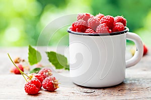 Fresh raspberries in white enamelled mug on table