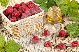 Fresh raspberries in a wicker box and honey, green leaves