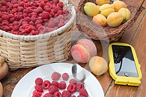 Fresh raspberry, peaches and Apricot, smartphone in a wicker basket on wooden table