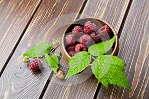 Fresh raspberry red berries with green leaves in bowl on wooden table