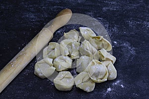 Fresh Ravioli with a wood kneader on floury dark background. Italian homemade healthy food concept.Process of making italian