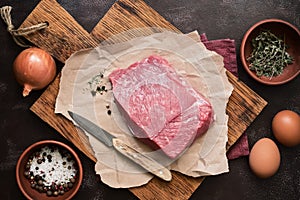 Fresh raw beef fillet and ingredients for the preparation of minced meat, egg, onion, spices on a dark background. Top view, flat