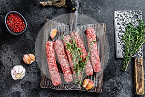 Fresh raw beef meat kebabs sausages on a cutting board. Black background. Top view