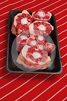 Fresh raw beef ox tail cuts on a black plastic trey and red and white butcher apron.