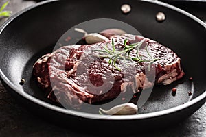 Fresh raw beef Ribe Eye steak in teflon pan with rosemary, garlic, salt and pepper