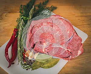 Fresh raw beef on wooden cutting board, spices and herbs. Whole uncooked beef prepare for cooking.