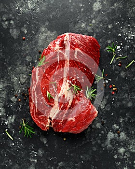 Fresh Raw braising steak on black background with rosemary, pepper, salt
