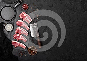 Fresh raw butchers lamb beef cutlets on stone board with vintage hatchet on black stone background. Salt and pepper with pan