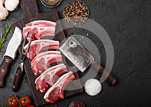 Fresh raw butchers lamb beef cutlets on stone board with vintage meat fork and knife and hatchet on black background.Salt, pepper