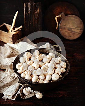 Fresh raw champignons in an iron bowl on a dark wooden table