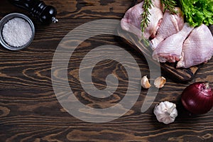 Fresh raw chicken drumstick and thigh on a board with spices and herbs on a wooden table