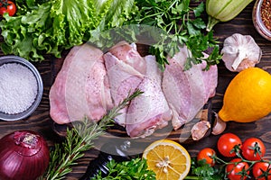 Fresh raw chicken drumstick and thigh on a board with spices and herbs on a wooden table