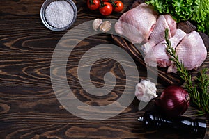 Fresh raw chicken drumstick and thigh on a board with spices and herbs on a wooden table