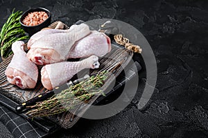 Fresh Raw chicken drumsticks legs on wooden cutting board. Black background. Top view. Copy space